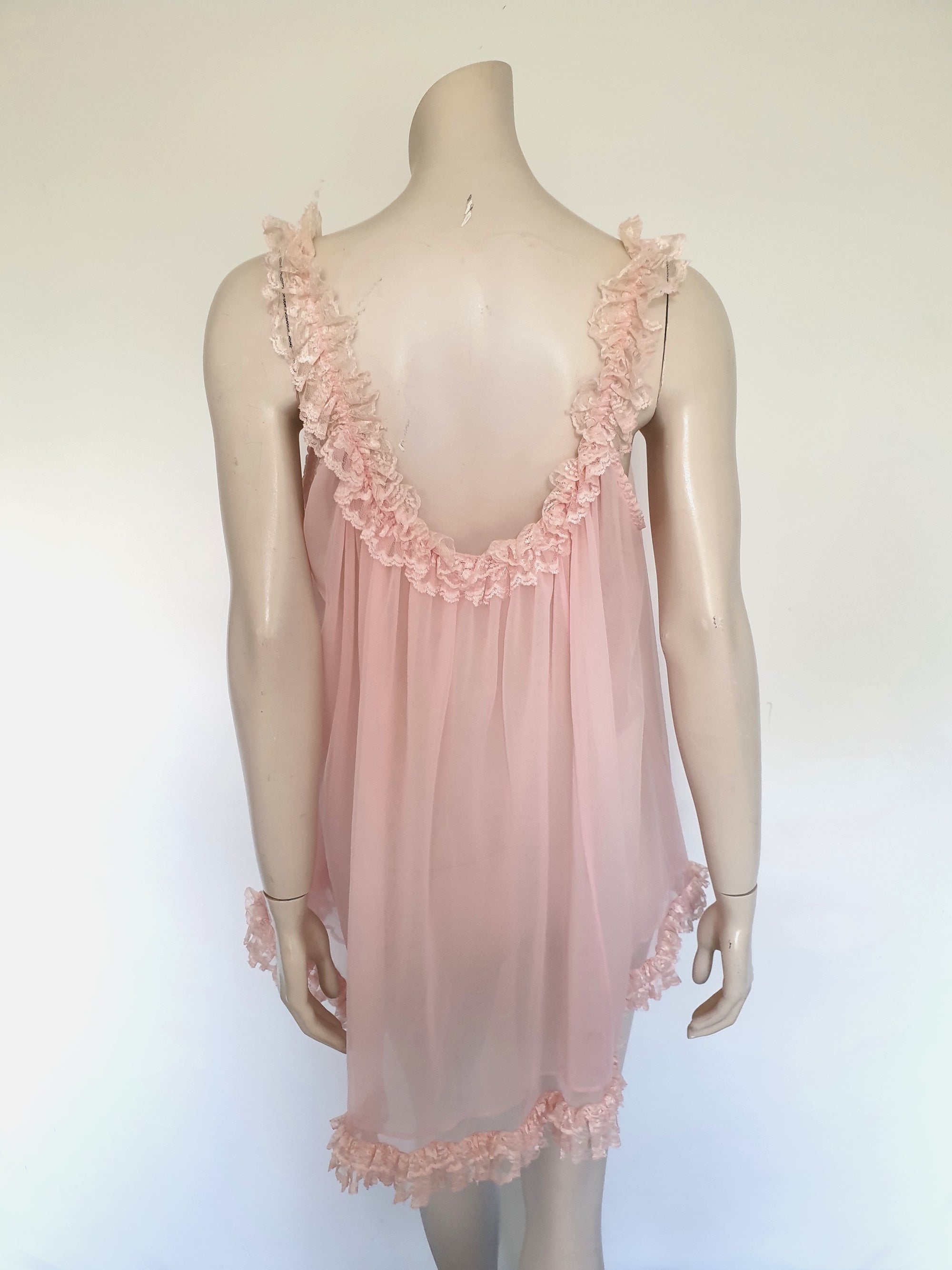 Pink Babydoll has a wide scooped neckline extending into straps. The neckline and the straps are  on elastic and are trimmed with wide ruffled lace. The same lace trims the hem. Ribbon bow at the front. The underarms are also elasticised. It's made from two layers of sheer nylon. Label reads S.G. for Escante, and appears to be a reproduction of the popular '60 style made likely in the 1990s. Extra large, marked 3XL