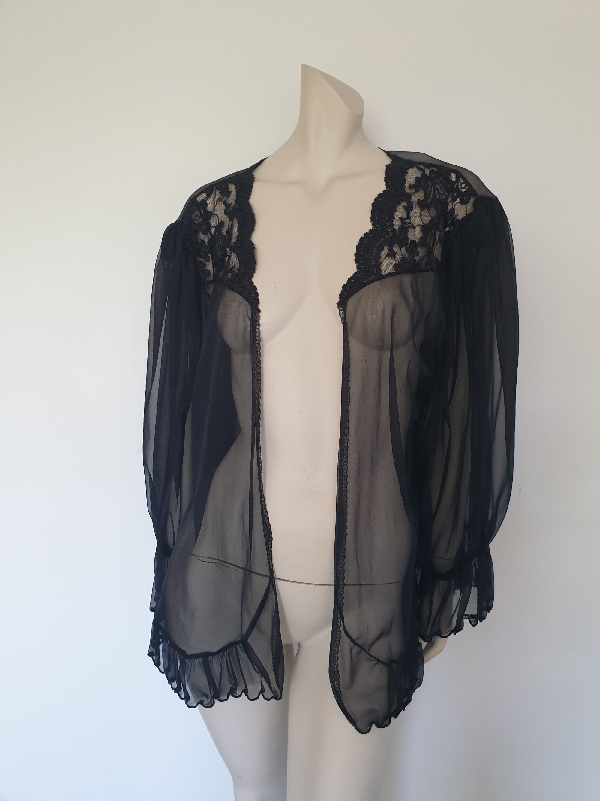 Sheer black mini length robe has long, gathered sleeves with sleeve headers and elastic at the wrists. Lace panels at the front yoke and ruffled trim. Narrow lace trim at the front opening and neckline. No closure. Fabric is nylon. Label says S. G. for Escante. 1980s-1990s. Extra Large.