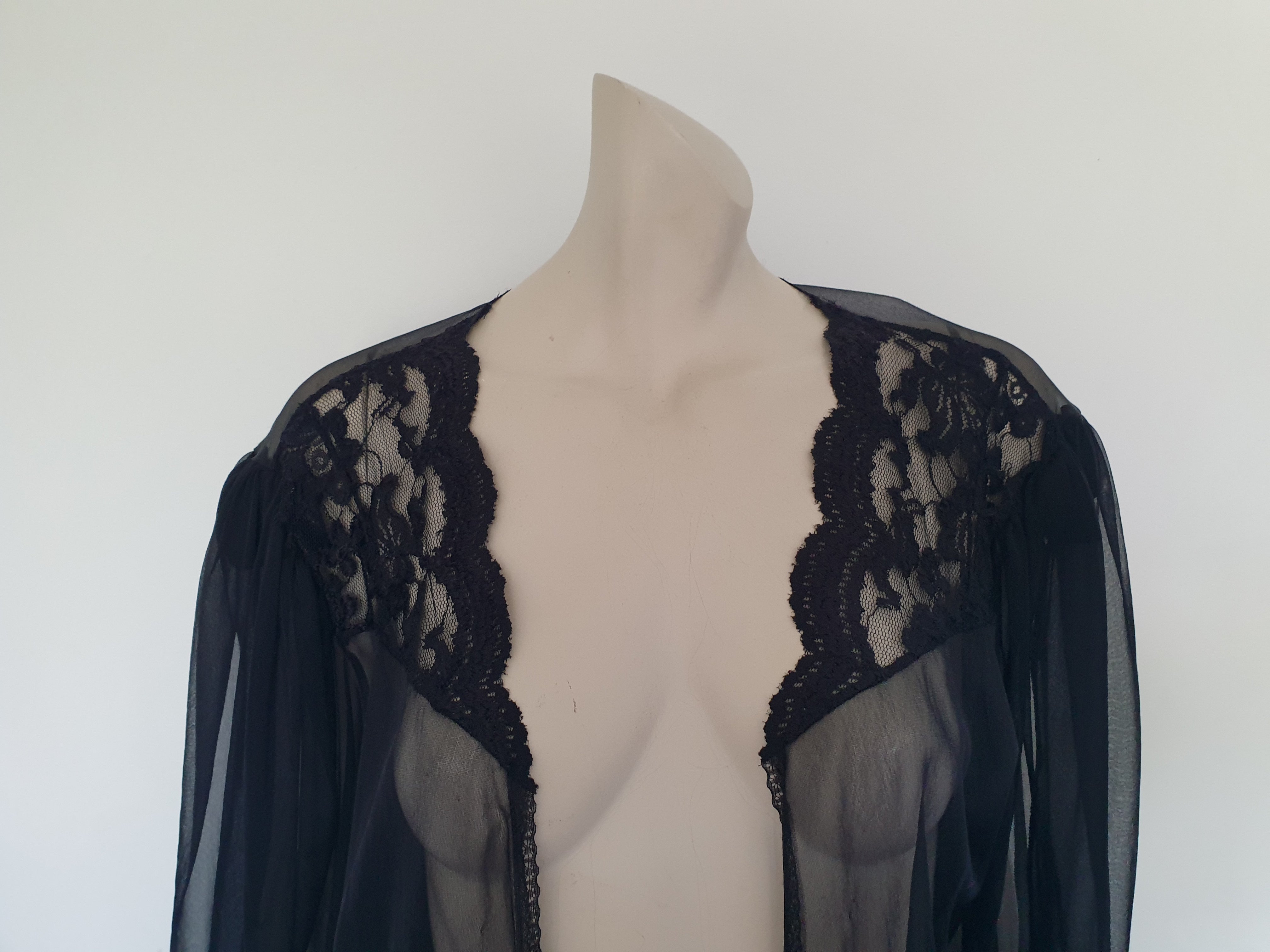 Sheer black mini length robe has long, gathered sleeves with sleeve headers and elastic at the wrists. Lace panels at the front yoke and ruffled trim. Narrow lace trim at the front opening and neckline. No closure. Fabric is nylon. Label says S. G. for Escante. 1980s-1990s. Extra Large.
