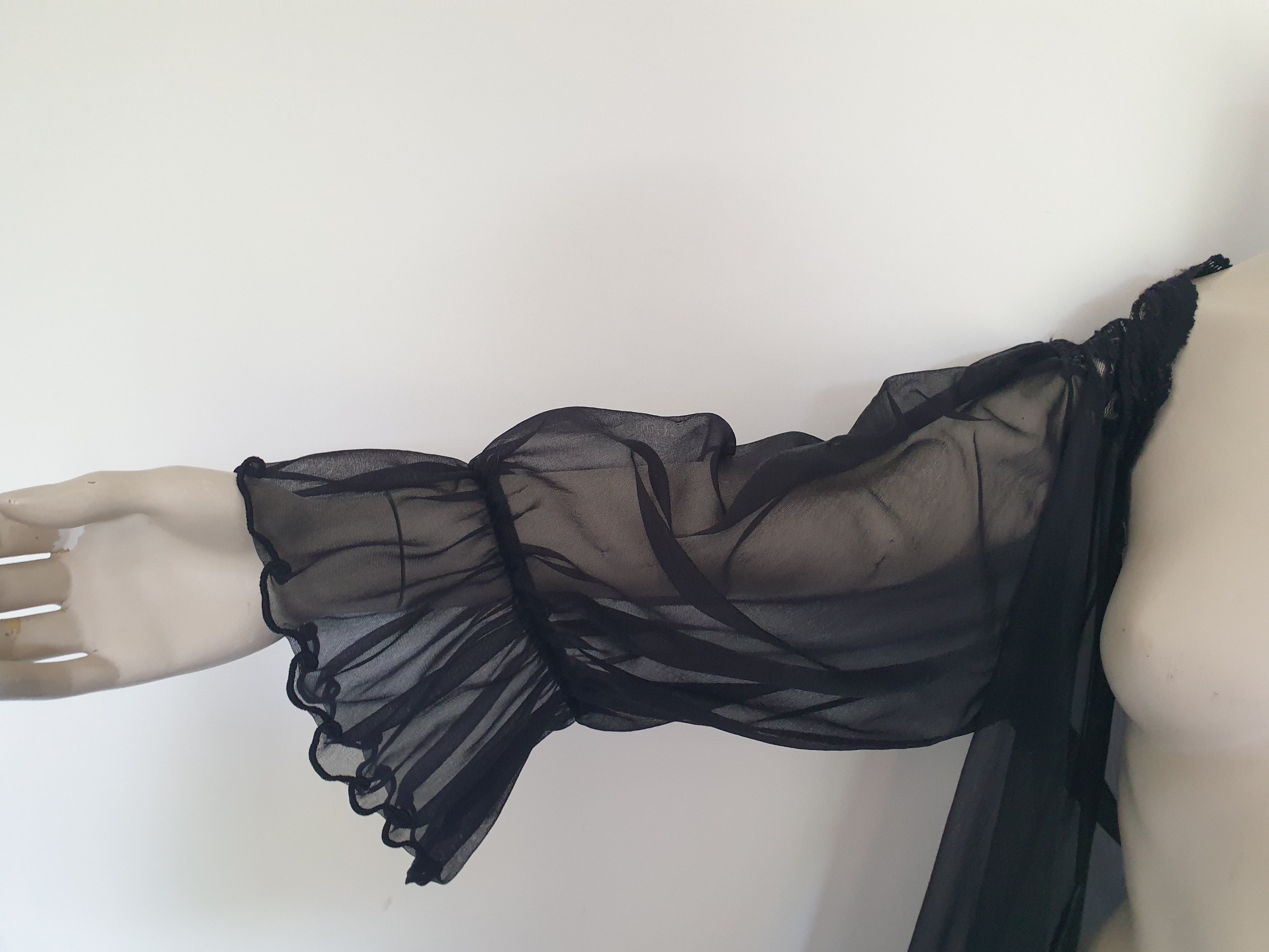 Sheer black mini length robe has long, gathered sleeves with sleeve headers and elastic at the wrists. Lace panels at the front yoke and ruffled trim. Narrow lace trim at the front opening and neckline. No closure. Fabric is nylon. Label says S. G. for Escante. 1980s-1990s. Extra Large.