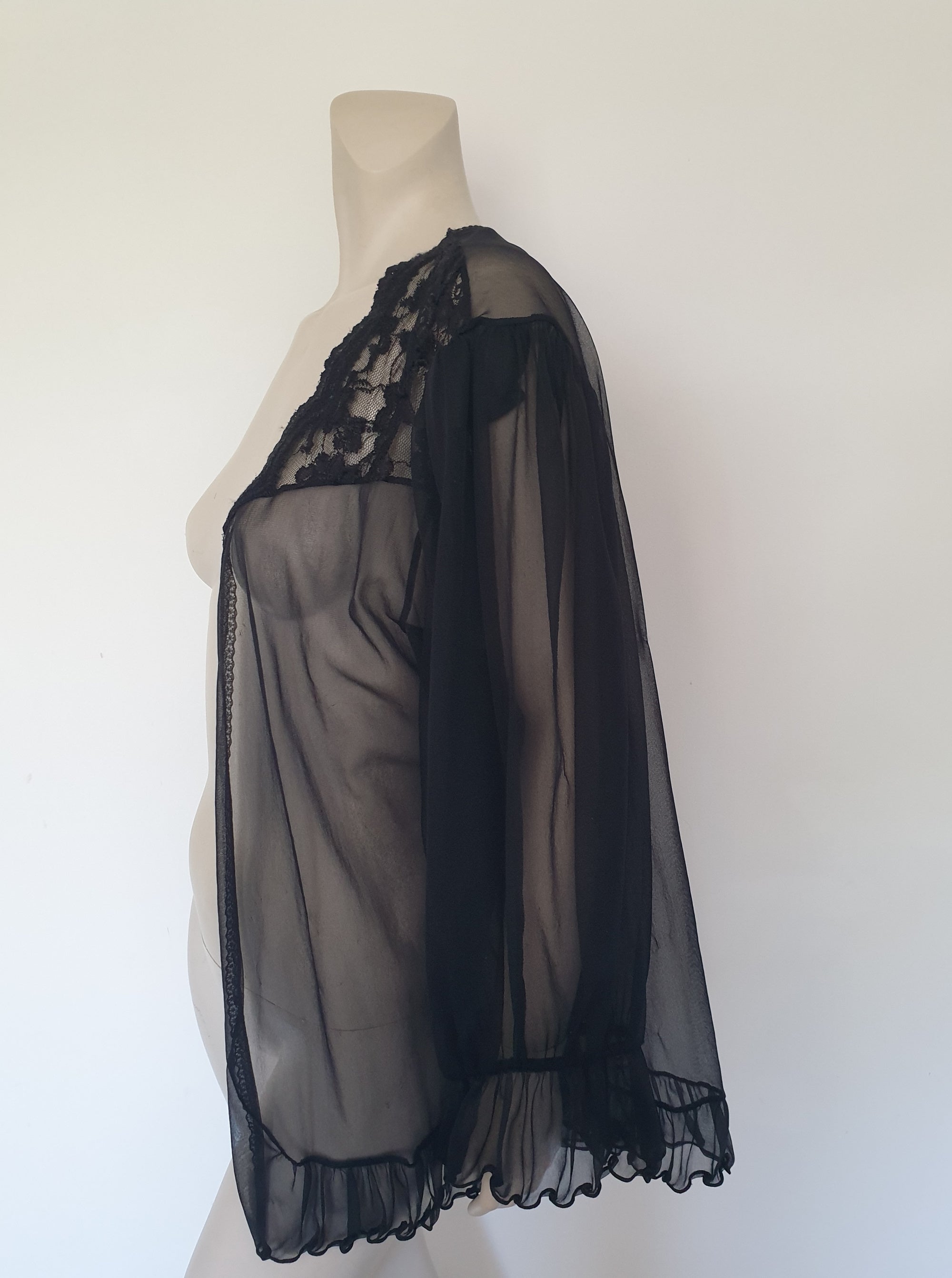 Sheer black mini length robe has long, gathered sleeves with sleeve headers and elastic at the wrists. Lace panels at the front yoke and ruffled trim. Narrow lace trim at the front opening and neckline. No closure. Fabric is nylon. Label says S. G. for Escante. 1980s-1990s. Extra Large.