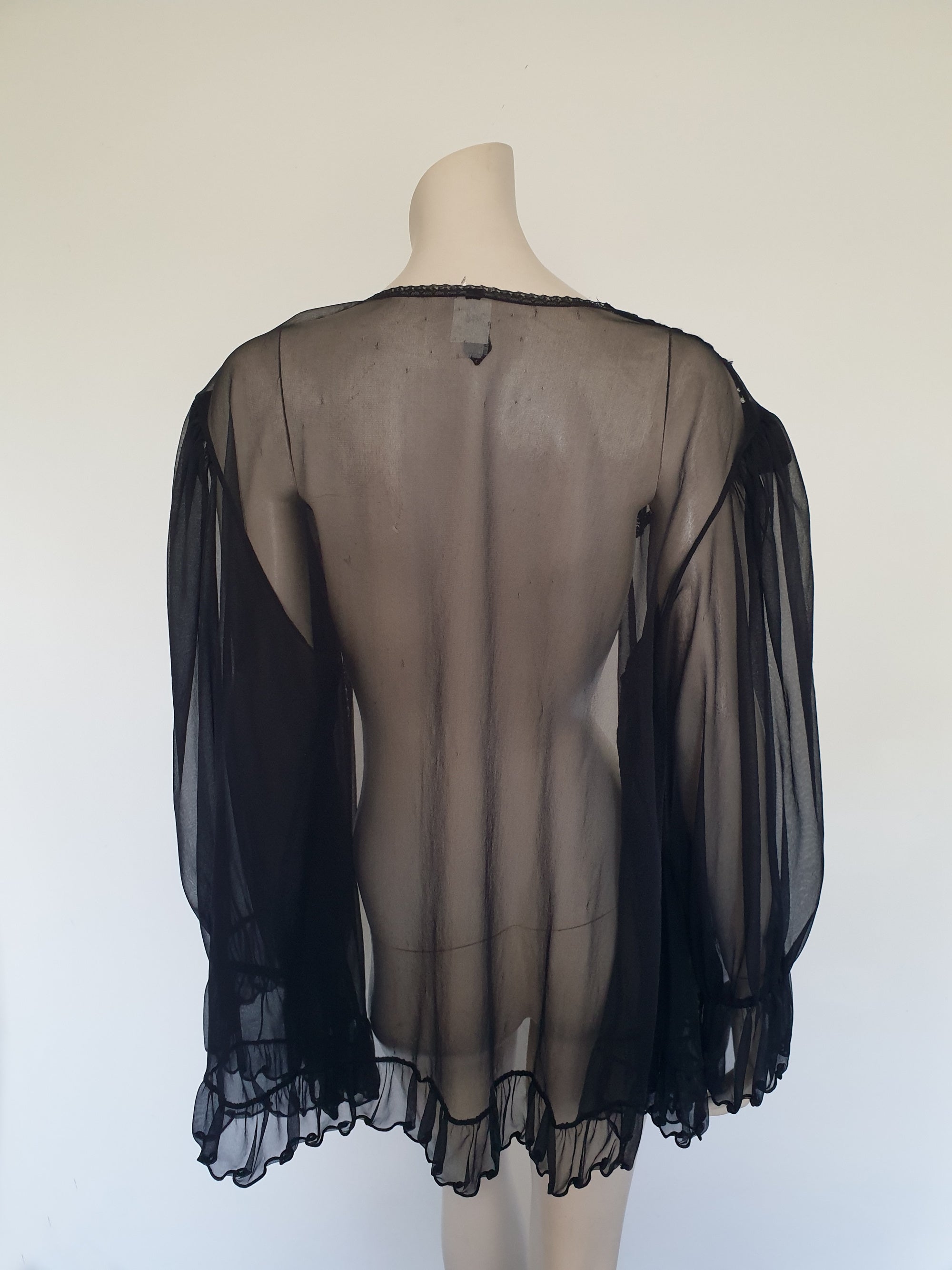 Sheer black mini length robe has long, gathered sleeves with sleeve headers and elastic at the wrists. Lace panels at the front yoke and ruffled trim. Narrow lace trim at the front opening and neckline. No closure. Fabric is nylon. Label says S. G. for Escante. 1980s-1990s. Extra Large.