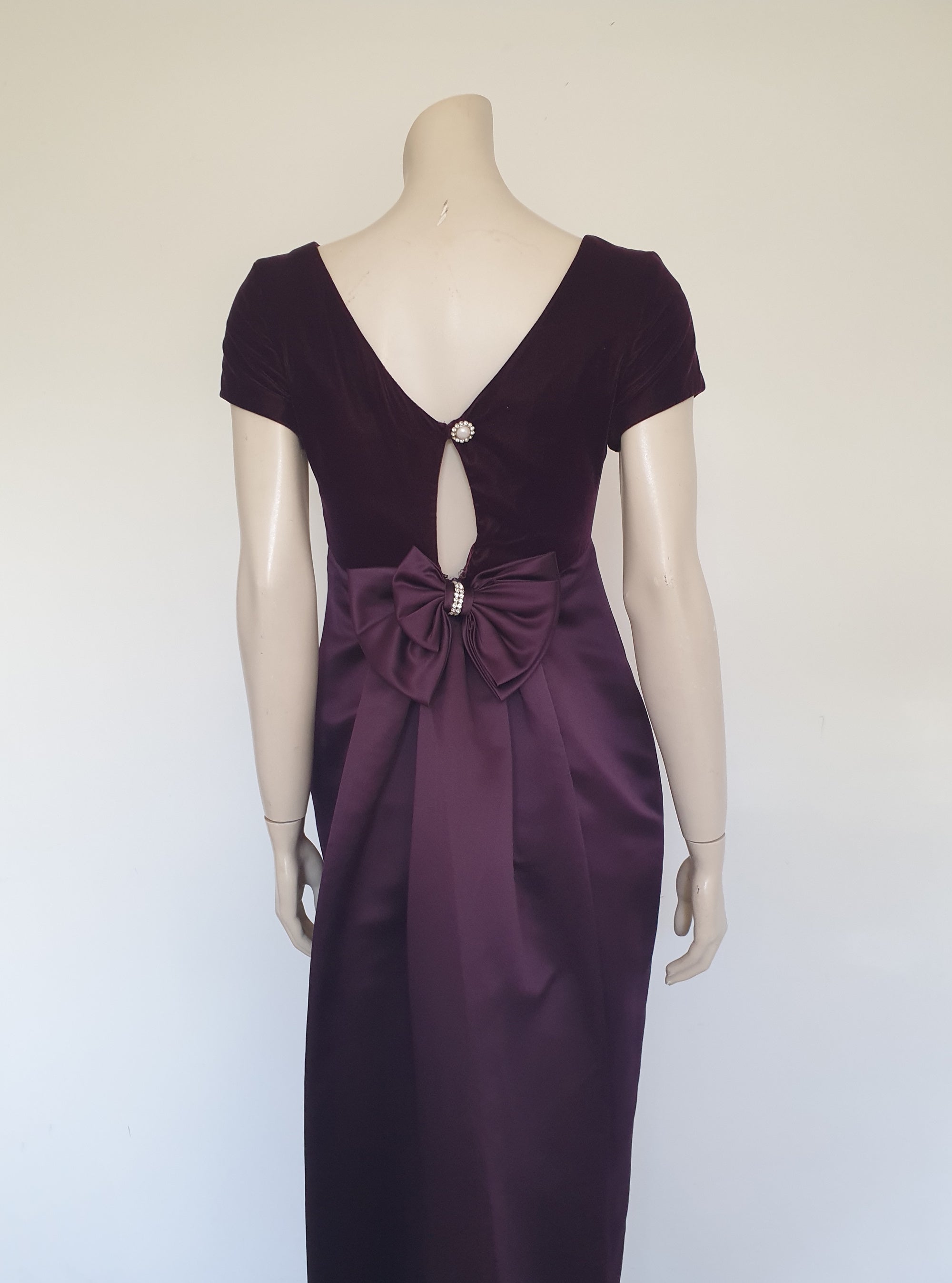 Beautiful and elegant aubergine formal sheath style gown with velvet bodice and stunning rear view. The gown has a wide neckline cut low at the back where it features a diamante studded bow extending into a narrow train over the the rear of the dress. Beneath the train the gown is slit to above the knee. The bodice is velvet and the satin skirt falls from beneath the bust. Closes at the back with a zip and a fancy button. Fabric is polyester. Made in Australia. Brand is Aurelie - 1980s. XS