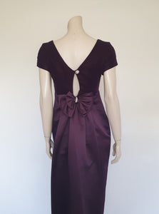 Beautiful and elegant aubergine formal sheath style gown with velvet bodice and stunning rear view. The gown has a wide neckline cut low at the back where it features a diamante studded bow extending into a narrow train over the the rear of the dress. Beneath the train the gown is slit to above the knee. The bodice is velvet and the satin skirt falls from beneath the bust. Closes at the back with a zip and a fancy button. Fabric is polyester. Made in Australia. Brand is Aurelie - 1980s. XS