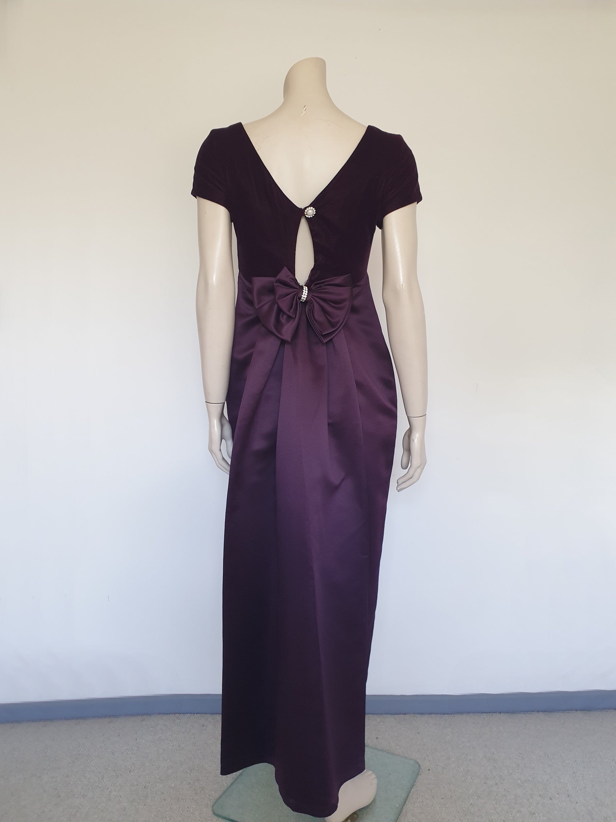 Beautiful and elegant aubergine formal sheath style gown with velvet bodice and stunning rear view. The gown has a wide neckline cut low at the back where it features a diamante studded bow extending into a narrow train over the the rear of the dress. Beneath the train the gown is slit to above the knee. The bodice is velvet and the satin skirt falls from beneath the bust. Closes at the back with a zip and a fancy button. Fabric is polyester. Made in Australia. Brand is Aurelie - 1980s. XS