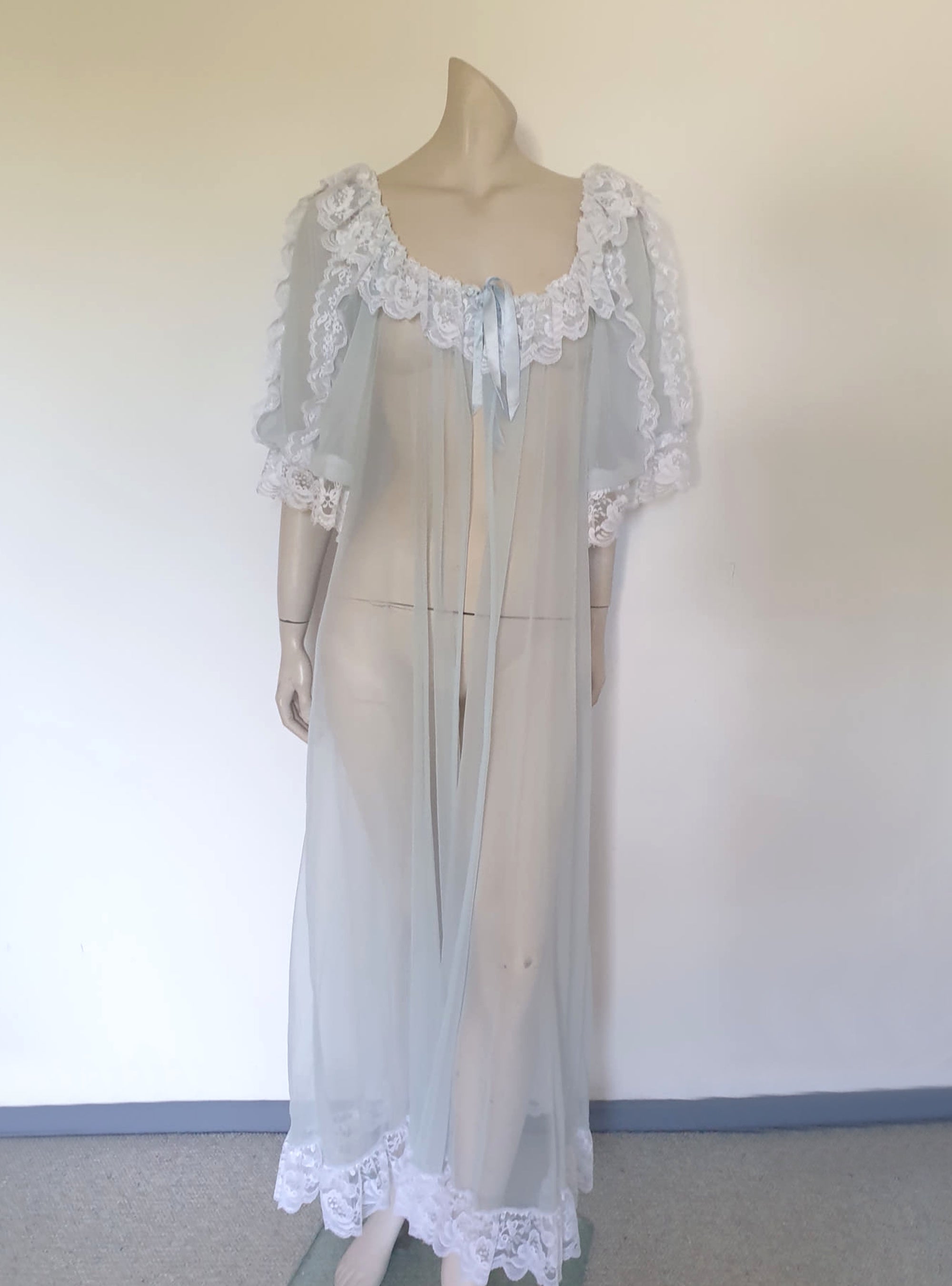 Sheer and sexy vintage glamour. This beautiful peignoir or robe is pale aqua or blue depending on the light, and is trimmed with white white lace. Low, scooped neckline at the front and back. The wide, full sleeves come to below the elbow . Open at the front and ties at the breast with a ribbon. Fabric is nylon. The labels have been removed. 1960s. Medium