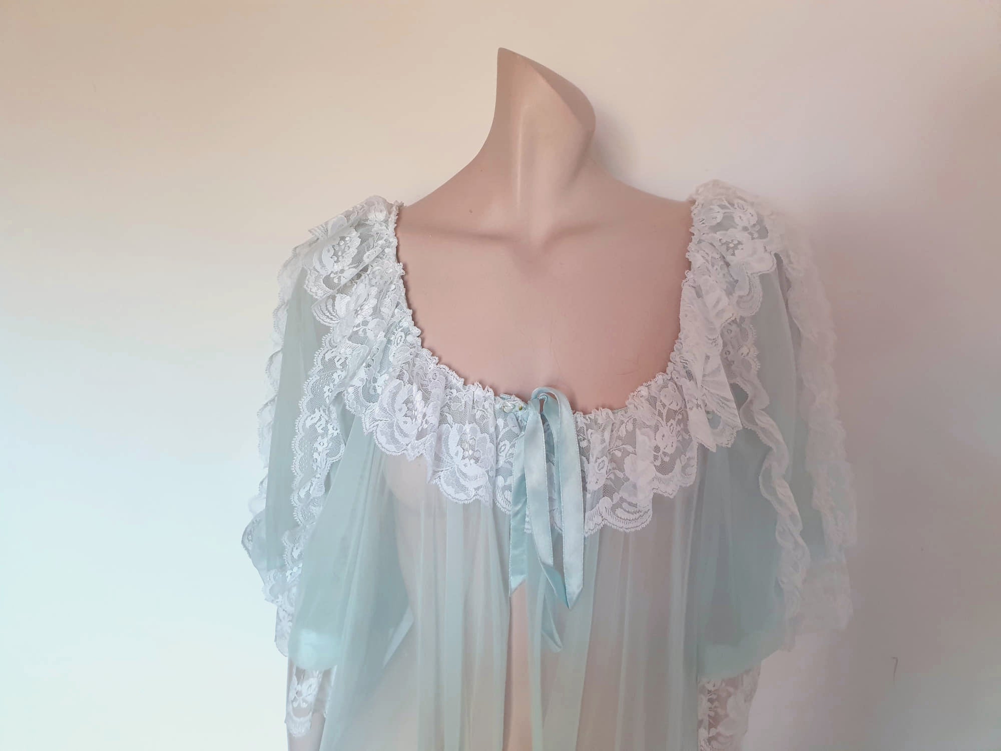 Sheer and sexy vintage glamour. This beautiful peignoir or robe is pale aqua or blue depending on the light, and is trimmed with white white lace. Low, scooped neckline at the front and back. The wide, full sleeves come to below the elbow . Open at the front and ties at the breast with a ribbon. Fabric is nylon. The labels have been removed. 1960s. Medium