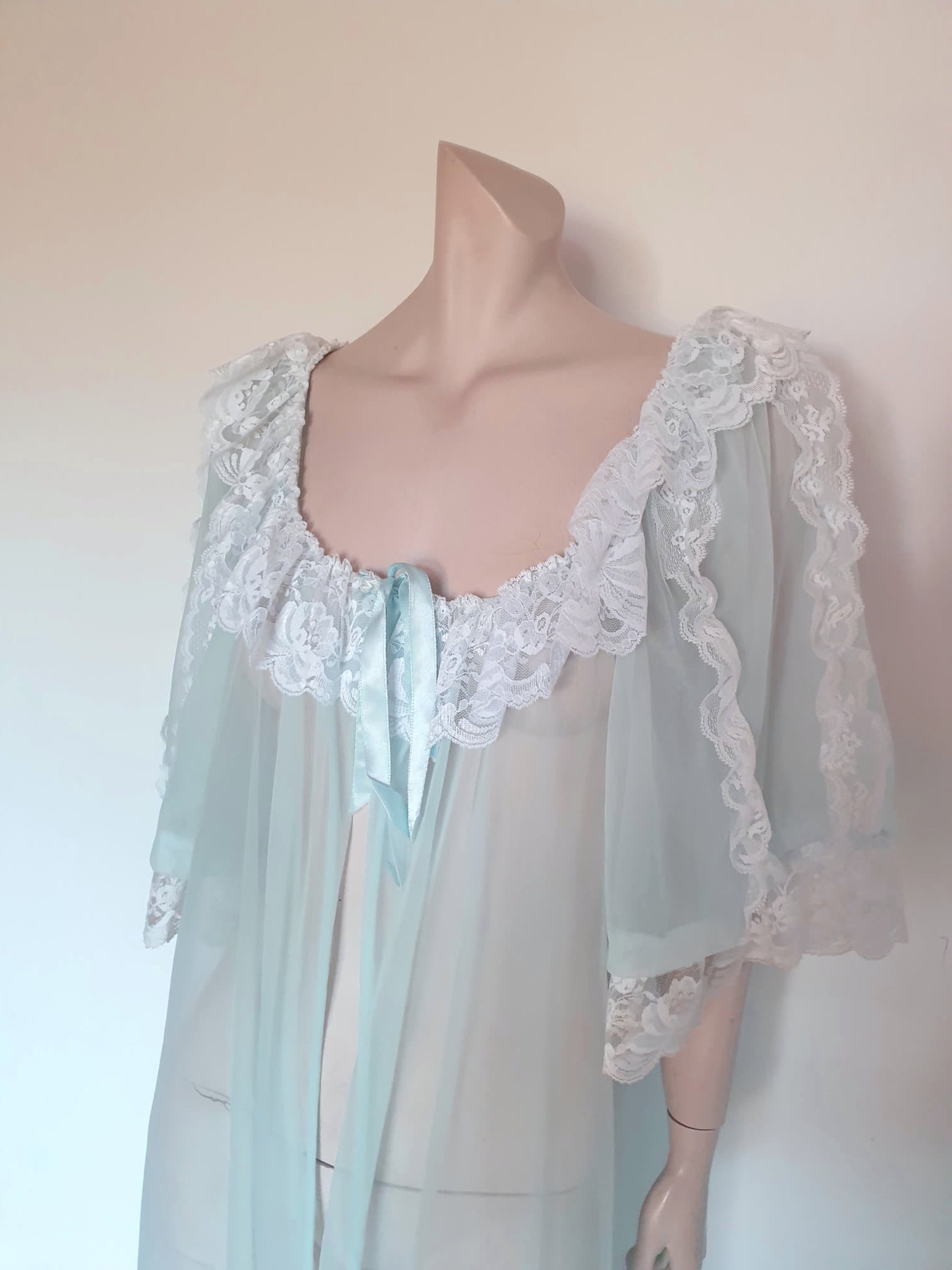 Sheer and sexy vintage glamour. This beautiful peignoir or robe is pale aqua or blue depending on the light, and is trimmed with white white lace. Low, scooped neckline at the front and back. The wide, full sleeves come to below the elbow . Open at the front and ties at the breast with a ribbon. Fabric is nylon. The labels have been removed. 1960s. Medium