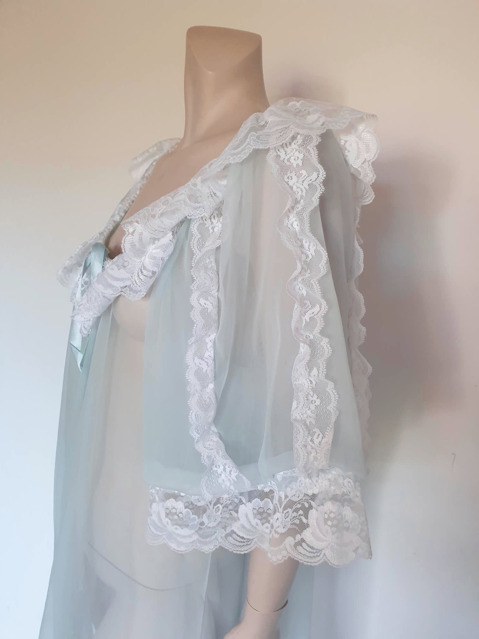 Sheer and sexy vintage glamour. This beautiful peignoir or robe is pale aqua or blue depending on the light, and is trimmed with white white lace. Low, scooped neckline at the front and back. The wide, full sleeves come to below the elbow . Open at the front and ties at the breast with a ribbon. Fabric is nylon. The labels have been removed. 1960s. Medium