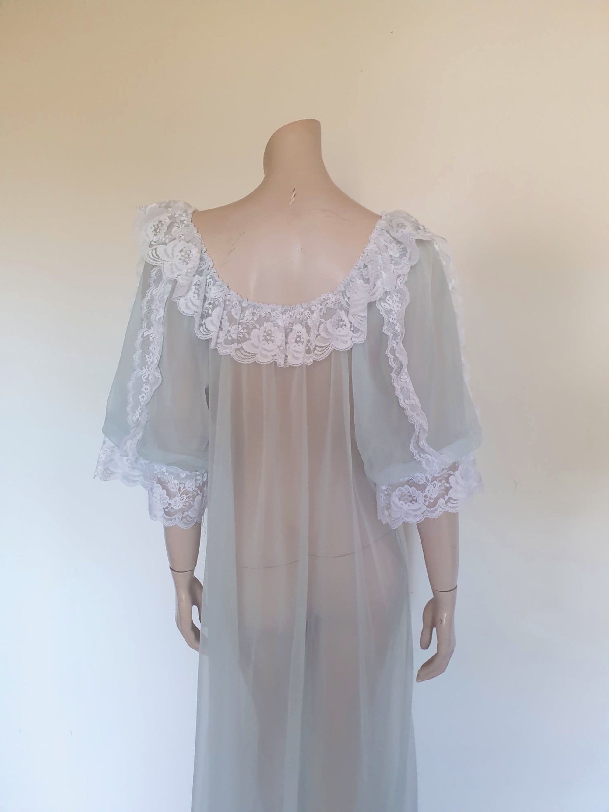 Sheer and sexy vintage glamour. This beautiful peignoir or robe is pale aqua or blue depending on the light, and is trimmed with white white lace. Low, scooped neckline at the front and back. The wide, full sleeves come to below the elbow . Open at the front and ties at the breast with a ribbon. Fabric is nylon. The labels have been removed. 1960s. Medium