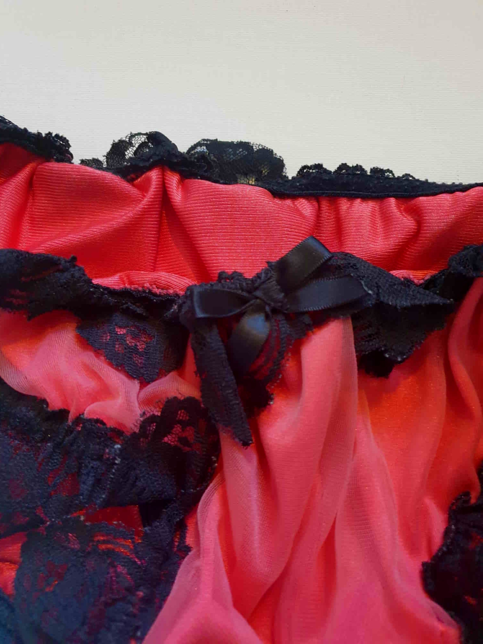 Red bikini style sleepwear panties, most likely worn with a babydoll, sheer gown or PJ top. These have a sheer nylon overlay and are trimmed with wide, scalloped black lace and a ribbon bow. No cotton gusset. Fabric is nylon. There are no tags. Medium