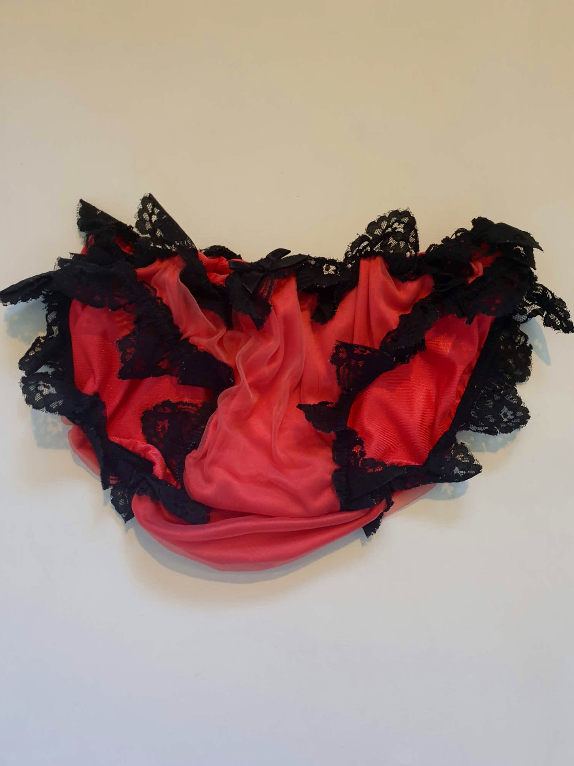Red bikini style sleepwear panties, most likely worn with a babydoll, sheer gown or PJ top. These have a sheer nylon overlay and are trimmed with wide, scalloped black lace and a ribbon bow. No cotton gusset. Fabric is nylon. There are no tags. Medium