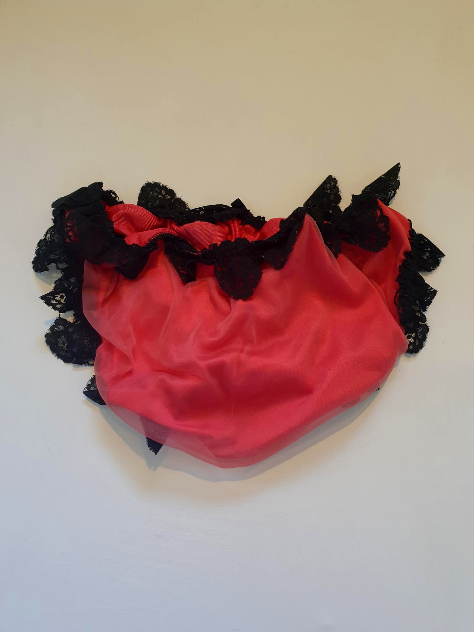Red bikini style sleepwear panties, most likely worn with a babydoll, sheer gown or PJ top. These have a sheer nylon overlay and are trimmed with wide, scalloped black lace and a ribbon bow. No cotton gusset. Fabric is nylon. There are no tags. Medium
