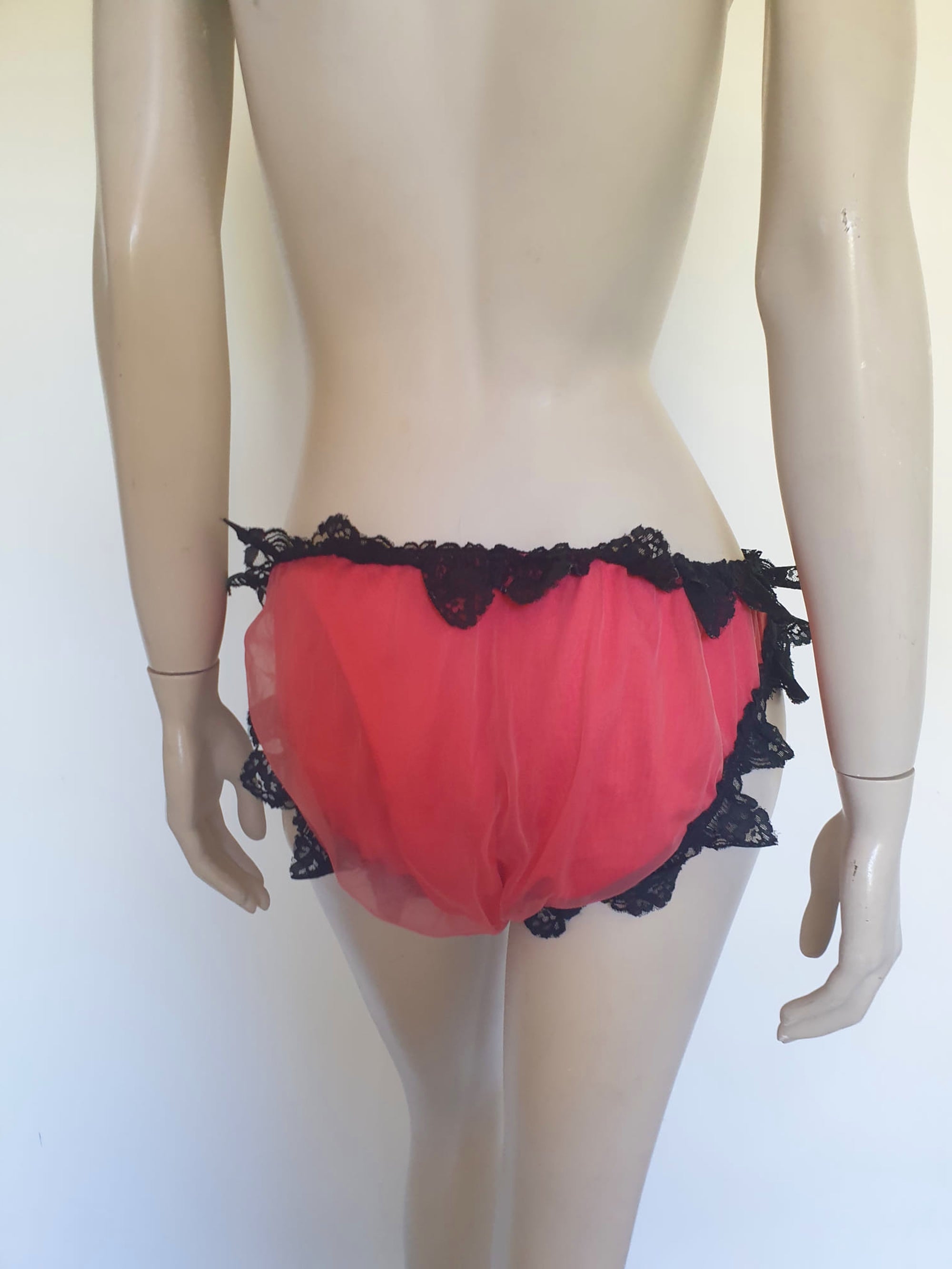 Red bikini style sleepwear panties, most likely worn with a babydoll, sheer gown or PJ top. These have a sheer nylon overlay and are trimmed with wide, scalloped black lace and a ribbon bow. No cotton gusset. Fabric is nylon. There are no tags. Medium