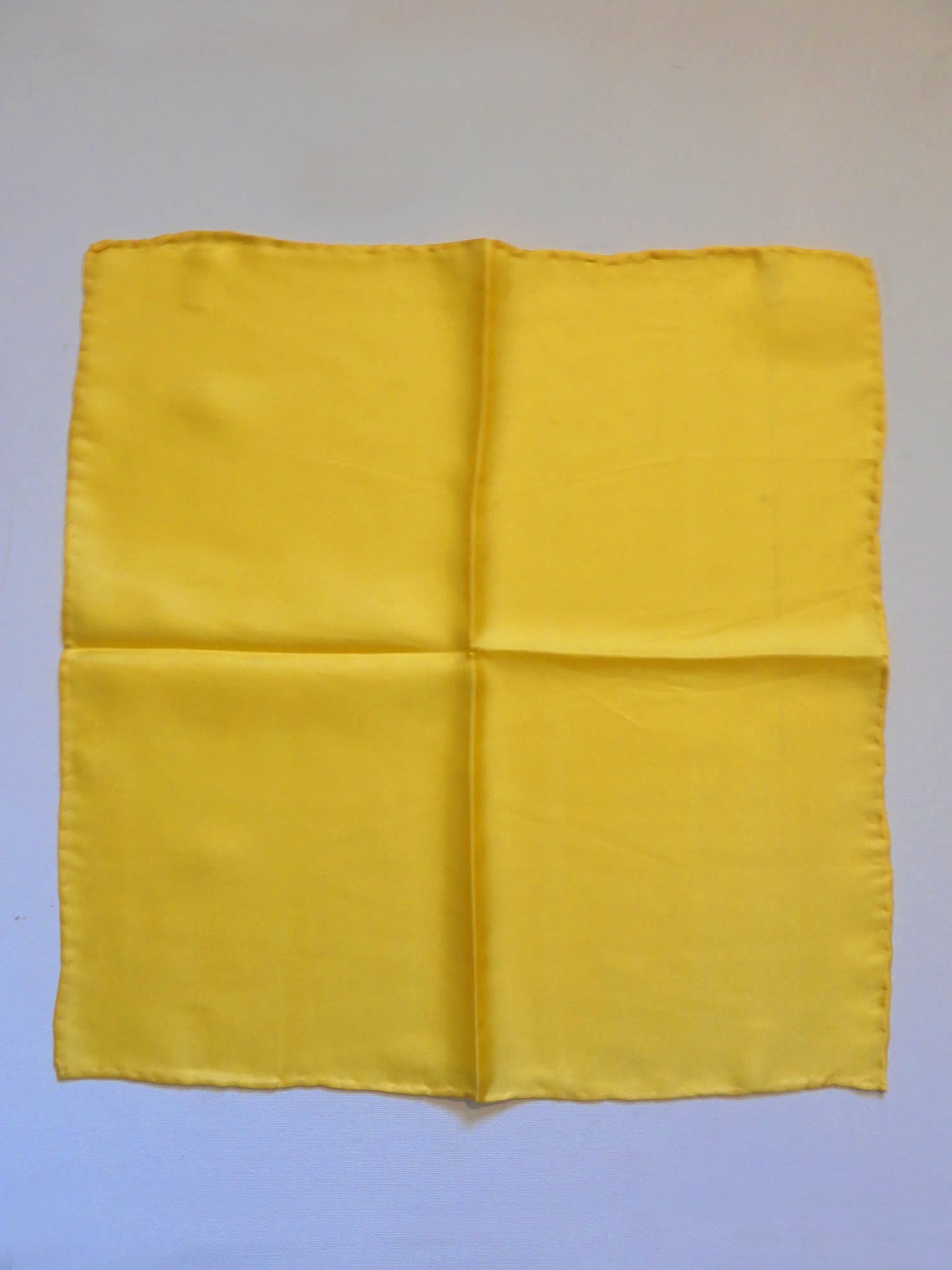 Yellow silk pocket square has hand rolled edges. Tag says 100% pure silk - Made in China.