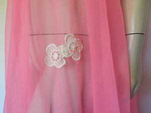 Super sexy sheer hot pink negligee nightgown. Has some issues but presents well. Very full negligee has wide neckline trimmed with cream lace. The hem is trimmed with a deep border of cream lace. There's a fixed tie at centre back which can tie in the fullness if you prefer. I have appliqued two flowers over two large holes in the front. Fabric is a single layer of sheer nylon. Made in the USA for Berkliff - 1960s. Small to Medium.