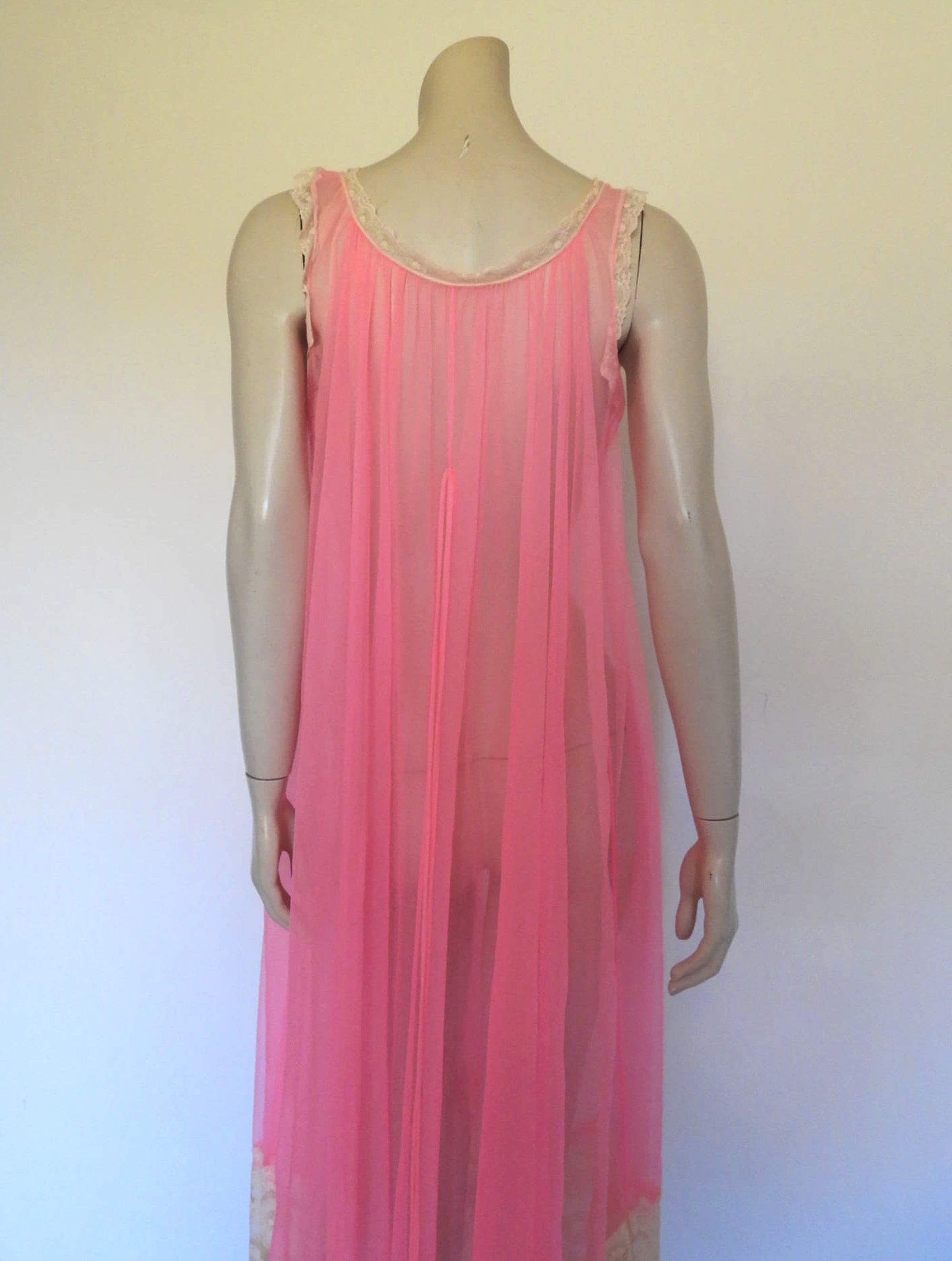 Super sexy sheer hot pink negligee nightgown. Has some issues but presents well. Very full negligee has wide neckline trimmed with cream lace. The hem is trimmed with a deep border of cream lace. There's a fixed tie at centre back which can tie in the fullness if you prefer. I have appliqued two flowers over two large holes in the front. Fabric is a single layer of sheer nylon. Made in the USA for Berkliff - 1960s. Small to Medium.