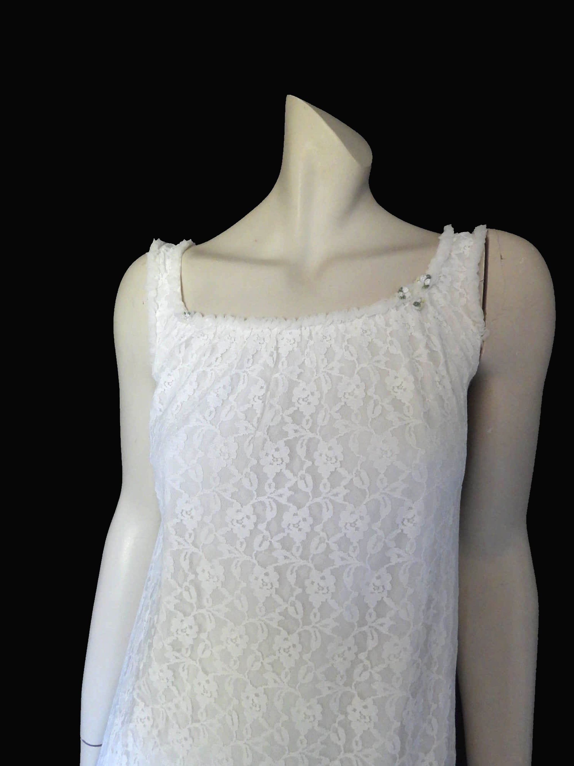 Pretty white lace knee-length nightgown would also make a sweet dress.
The nightie has scooped neckline front and back, horizontal tucks at the hem and ruffle trim at the neckline, armholes and hem. The neckline is trimmed with flower appliques. There is an opaque layer beneath the lace outer layer and this hangs down a little below the lace at the bottom. Nylon lace with acetate lining. Brand is St Mark, 1960s. Small.