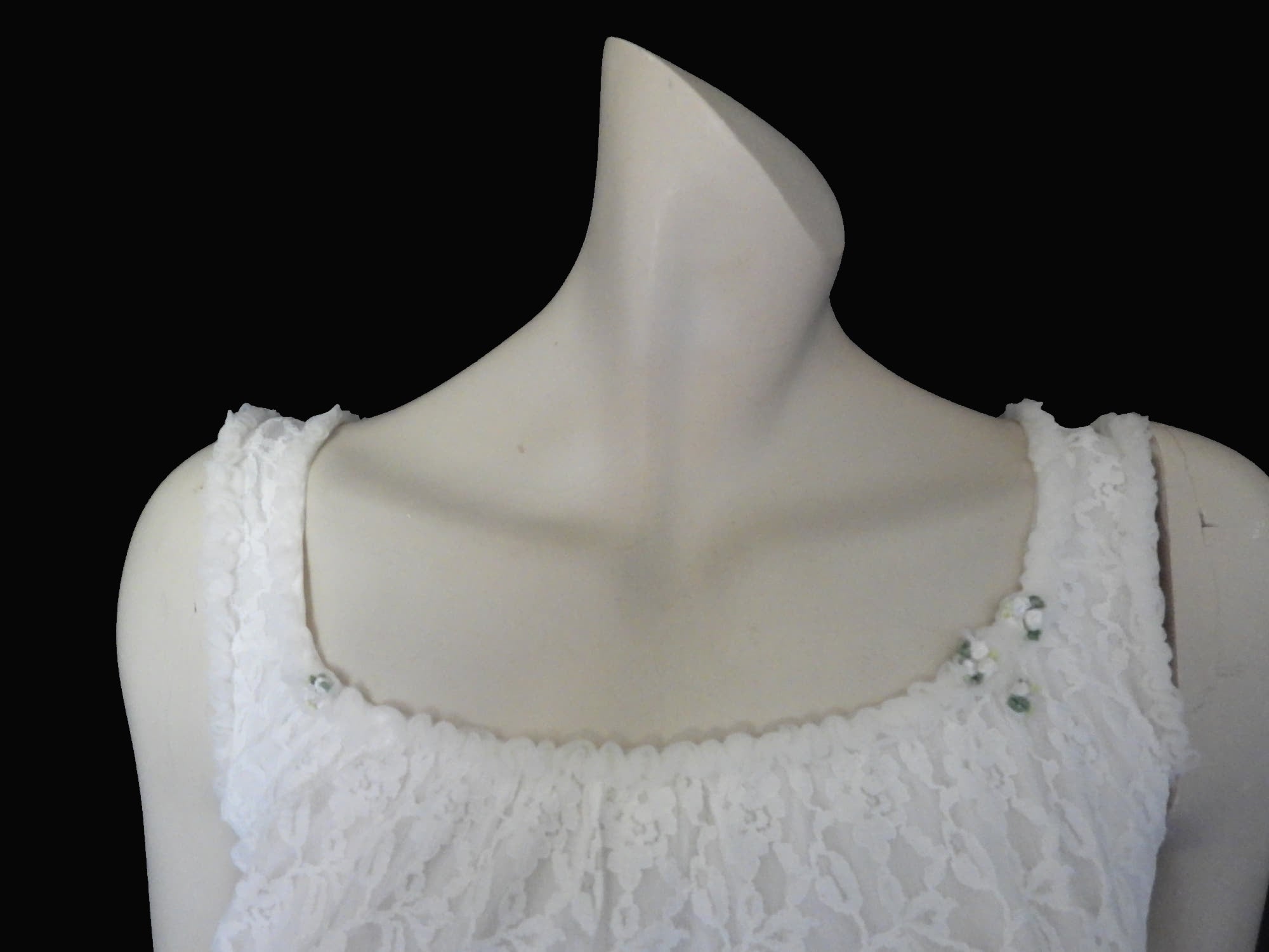 Pretty white lace knee-length nightgown would also make a sweet dress.
The nightie has scooped neckline front and back, horizontal tucks at the hem and ruffle trim at the neckline, armholes and hem. The neckline is trimmed with flower appliques. There is an opaque layer beneath the lace outer layer and this hangs down a little below the lace at the bottom. Nylon lace with acetate lining. Brand is St Mark, 1960s. Small.