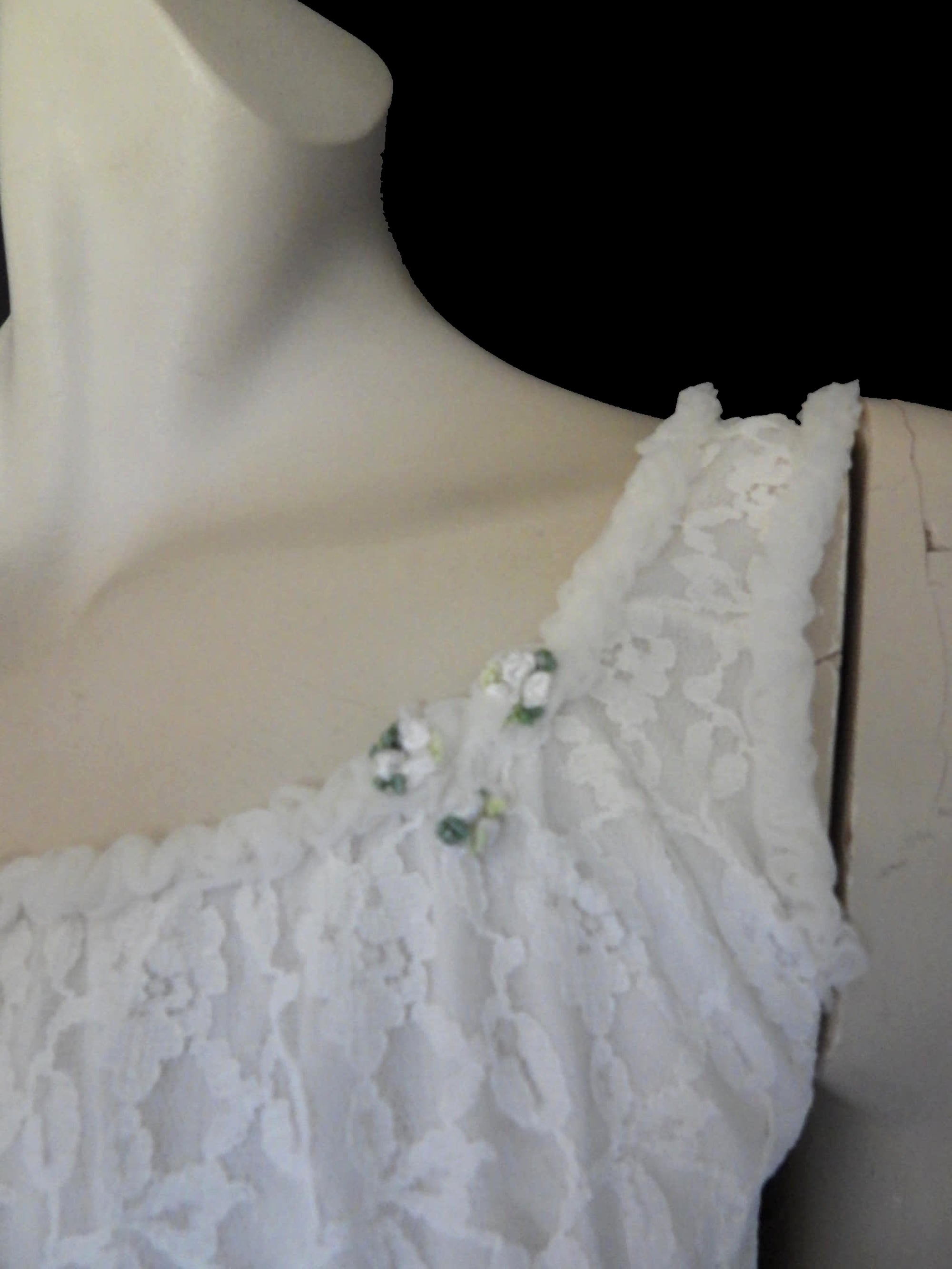 Pretty white lace knee-length nightgown would also make a sweet dress.
The nightie has scooped neckline front and back, horizontal tucks at the hem and ruffle trim at the neckline, armholes and hem. The neckline is trimmed with flower appliques. There is an opaque layer beneath the lace outer layer and this hangs down a little below the lace at the bottom. Nylon lace with acetate lining. Brand is St Mark, 1960s. Small.