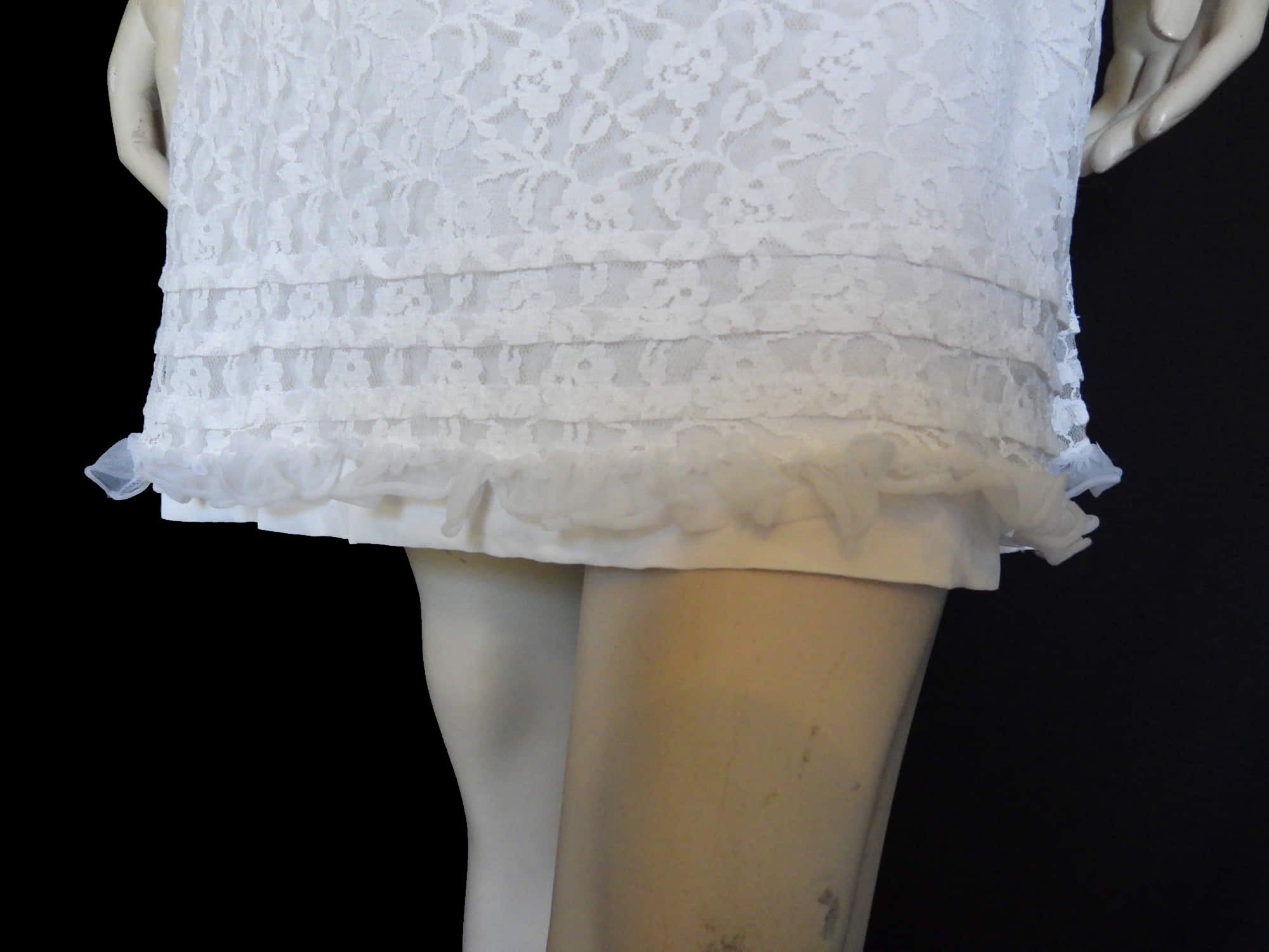 Pretty white lace knee-length nightgown would also make a sweet dress.
The nightie has scooped neckline front and back, horizontal tucks at the hem and ruffle trim at the neckline, armholes and hem. The neckline is trimmed with flower appliques. There is an opaque layer beneath the lace outer layer and this hangs down a little below the lace at the bottom. Nylon lace with acetate lining. Brand is St Mark, 1960s. Small.