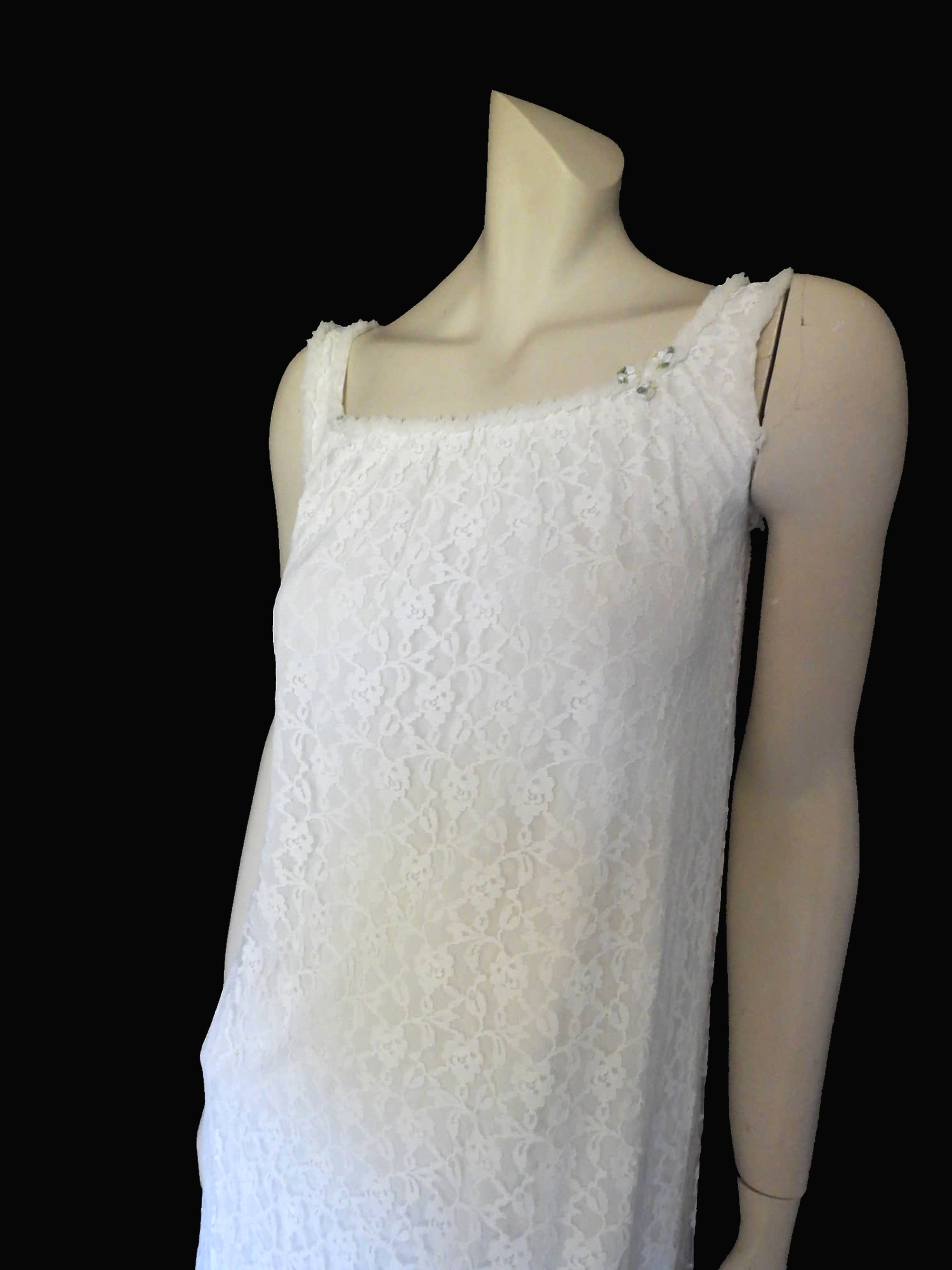 Pretty white lace knee-length nightgown would also make a sweet dress.
The nightie has scooped neckline front and back, horizontal tucks at the hem and ruffle trim at the neckline, armholes and hem. The neckline is trimmed with flower appliques. There is an opaque layer beneath the lace outer layer and this hangs down a little below the lace at the bottom. Nylon lace with acetate lining. Brand is St Mark, 1960s. Small.