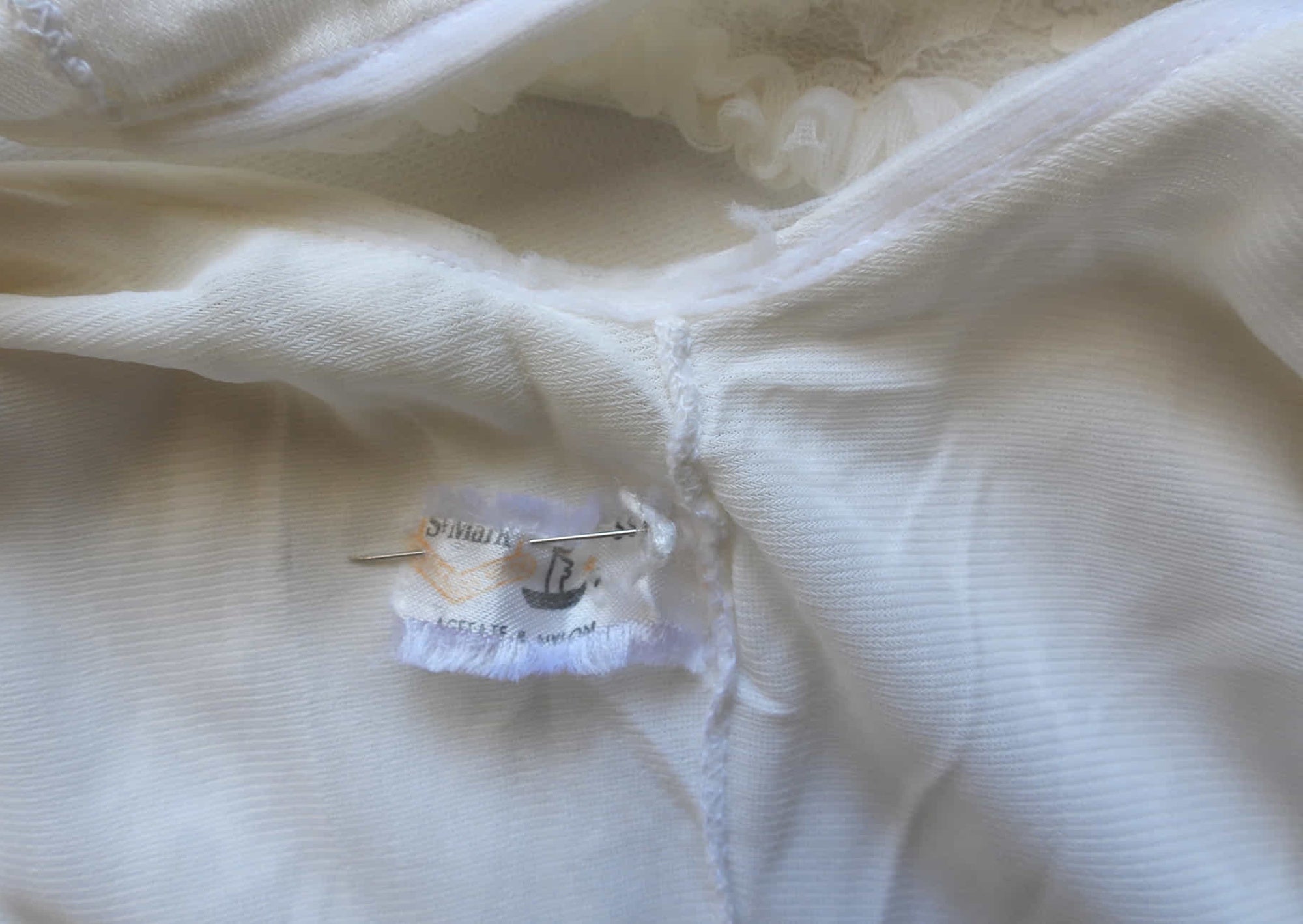 Pretty white lace knee-length nightgown would also make a sweet dress.
The nightie has scooped neckline front and back, horizontal tucks at the hem and ruffle trim at the neckline, armholes and hem. The neckline is trimmed with flower appliques. There is an opaque layer beneath the lace outer layer and this hangs down a little below the lace at the bottom. Nylon lace with acetate lining. Brand is St Mark, 1960s. Small.