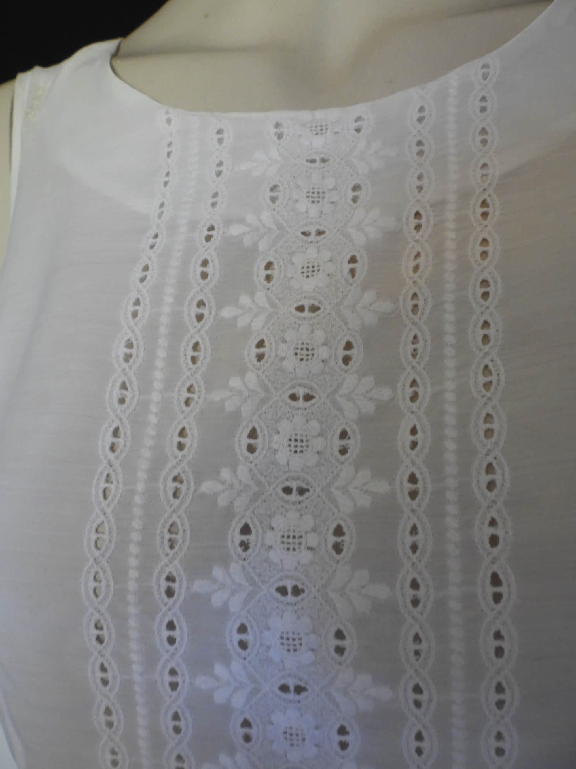 Tennis dress is decorated at centre front with eyelet embroidery. It has princess seaming and closes at the back with a zipper. The dress is semi sheer. The fabric appears to be an early form of polyester or maybe nylon, there's no fabric tag. The label reads "A Belle Garment Exclusive Model" - early 1960s. Medium