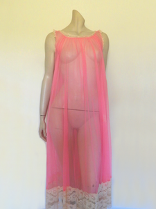 Super sexy sheer hot pink negligee nightgown. Has some issues but presents well. Very full negligee has wide neckline trimmed with cream lace. The hem is trimmed with a deep border of cream lace. There's a fixed tie at centre back which can tie in the fullness if you prefer. I have appliqued two flowers over two large holes in the front. Fabric is a single layer of sheer nylon. Made in the USA for Berkliff - 1960s. Small to Medium.