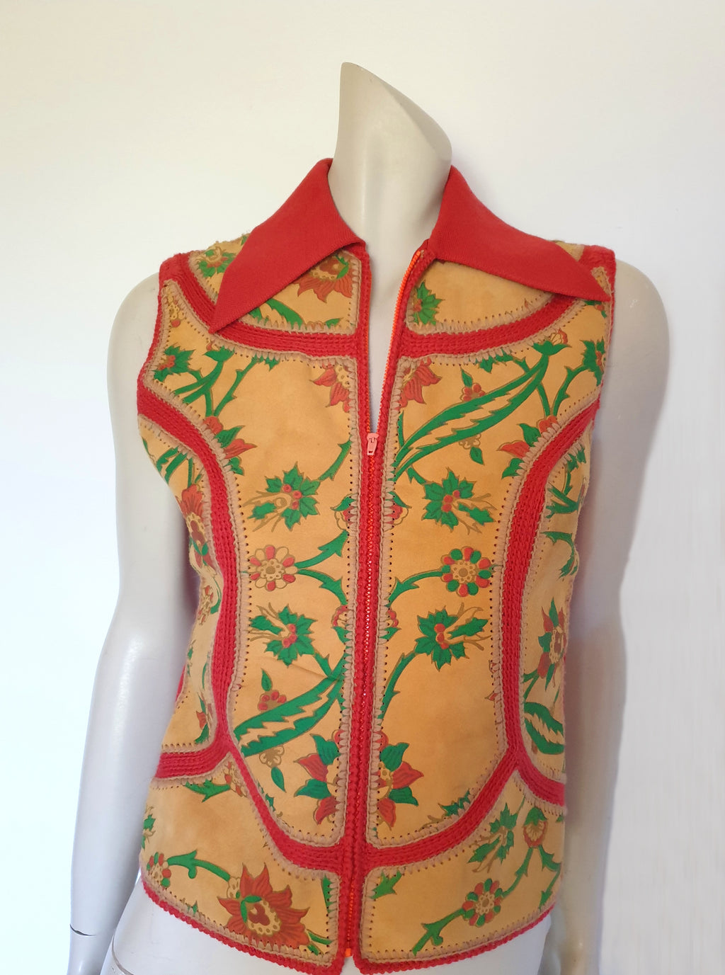 The long pointed collar and back of this wonderful piece are a burnt orange knit fabric. The same colour yarn is used to crochet the suede panels together. The suede has been hand painted or printed with a green and orange floral design. The front panels are lined with rayon. Closes with a zip in the front. There is no brand label. Made in Hong Kong, late 1960s or early 1970s. Small.